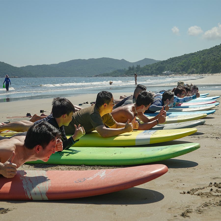 A group of beginner surfers learning how to surf and lying down on their boards on the beach.
